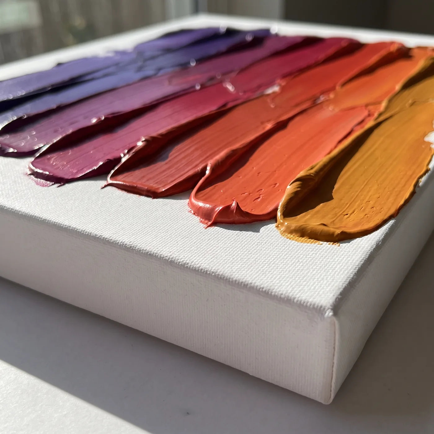 A 3D vászon éle oldalról — 4 cm mély fehér oldal és spatulával felhordott sűrű akrilfesték sávjai, mindegyik más színben, együtt lilától borostyánig tartó átmenetet adva
